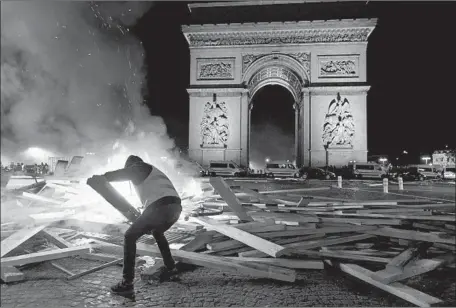  ?? Photograph­s by Bertrand Guay AFP/Getty Images ?? A DEMONSTRAT­OR with the Yellow Vests helps set fire to barricade material near the Arc de Triomphe. Thousands joined the protests.