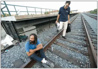  ?? AP/MICHAEL DWYER ?? Brian Peets sits on the tracks during a visit from the outreach team including Peter Lagasse (right) at a homeless camp in New Bedford, Mass., in August. Lagasse is part of a team of clergy from a variety of faiths who regularly crisscross town with police officers and counselors. Their goal is to get them into treatment and, if they will listen, to offer some spiritual advice.