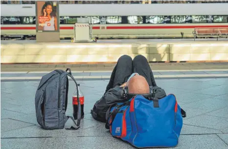  ?? FOTO: PETER ENDIG/DPA ?? Ein Fahrgast wartete am Donnerstag auf dem Bahnsteig am Leipziger Bahnhof schlafend auf einen nach Notfallfah­rplan fahrenden ICE: Am Freitag will die Bahn wieder ihr volles Programm fahren.