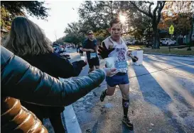  ?? Steve Gonzales / Houston Chronicle ?? A runner grabs water along University Boulevard, near the 10-mile mark. The marathon and half marathon attracted about 27,000 runners.