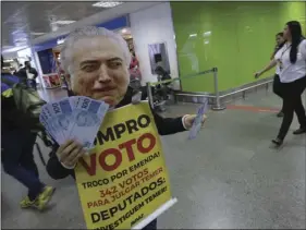  ??  ?? An activist protests, dressed with a mask of Brazil’s President Michel Temer, as he holds fake 100 Brazilian Real notes and a sign that reads in Portuguese “I buy votes,” at the arrivals area of the airport in Brasilia, Brazil on Tuesday. Temer faces a...