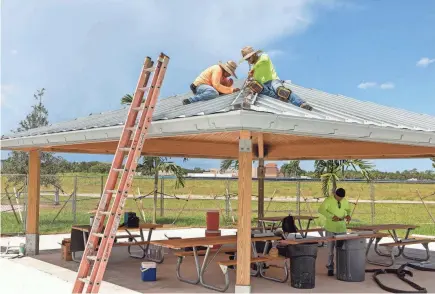  ?? GREG LOVETT/PALM BEACH POST ?? Decktight Roofing Services workers assemble a roof over picnic tables at the Canyon District Park in Boynton Beach in 2022. Another $13 million is needed to complete the park’s second phase.
