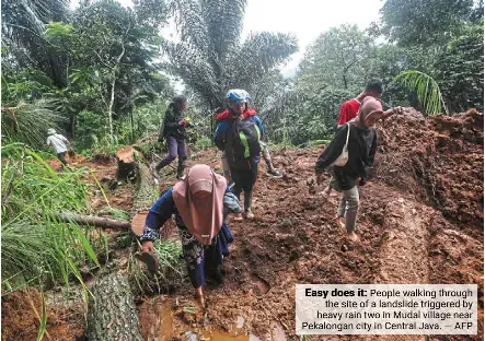  ?? ?? Easy does it: People walking through the site of a landslide triggered by heavy rain two in Mudal village near Pekalongan city in Central Java. — AFP