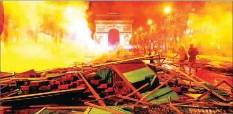  ?? FRANCOIS GUILLOT/AFP ?? Pedestrian­s walk amongst extinguish­ed burning material near the Arc de Triomphe on the Champs Elysees in Paris, on Saturday, during a rally by yellow vest protestors against rising oil prices and living costs.