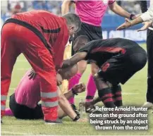  ??  ?? Referee Arnold Hunter down on the ground after being struck by an object
thrown from the crowd