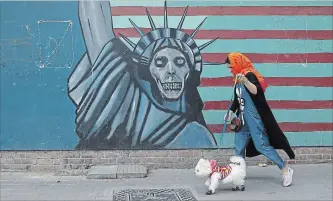  ?? VAHID SALEMI THE ASSOCIATED PRESS ?? A woman walks her dog past an anti-U.S. mural painted on the wall of the former American embassy in Tehran on Tuesday. Iran has not said how it will respond to the U.S. withdrawal from the 2015 nuclear deal.