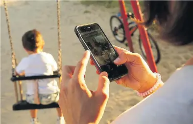  ?? JOSÉ LUIS ROCA ?? Una mujer pendiente de la pantalla de su teléfono móvil en un parque madrileño mientras un niño se columpia.