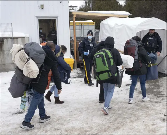  ?? RYAN REMIORZ — THE CANADIAN PRESS VIA AP ?? A family of asylum seekers from Columbia is met by Royal Canadian Mounted Police RCMP) officers after crossing the border into Canada Thursday. They are also heading into the U.S. too.