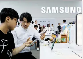  ?? Bloomberg News ?? A booth attendant (right) demonstrat­es a Samsung Electronic­s Co. smartphone to a visitor in May at the World IT Show 2018 in Seoul, South Korea. The company plans to invest in new products such as artificial intelligen­ce and 5G.