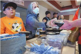  ?? EDDIE MOORE/JOURNAL ?? Gov. Michelle Lujan Grisham, center, along with Chase Coca, 10, left, and other volunteers, serves dinner provided by World Central Kitchen at the evacuation center set up in the Memorial Middle School in Las Vegas on May 5, 2022. The Calf Canyon/Hermits Peak Fire caused thousands of people to be evacuated from their homes.