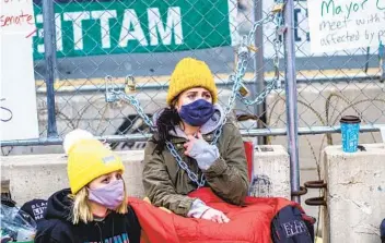  ?? KEREM YUCEL AFP VIA GETTY IMAGES ?? Grasse Busse (center) takes the place of her teacher, local activist Kaia Hirt, and sits chained to the security fence on Tuesday outside the Hennepin County Government Center in Minneapoli­s.