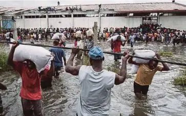  ??  ?? RATUSAN penduduk yang kelaparan memanjat dan mengambil beras dari sebuah gudang yang dikeliling­i air di Beira, Mozambique kelmarin. - AFP