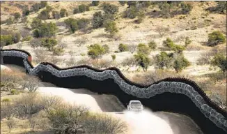  ?? Charlie Riedel Associated Press ?? A BORDER PATROL agent monitors the U.S. side of a border wall east of Nogales, Ariz. Border fencing has strengthen­ed drug cartels by increasing their incentives and economic rewards.