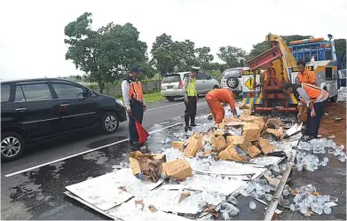  ?? EDI SUDRAJAT/JAWA POS ?? TRUK DIEVAKUASI DENGAN MOBIL DEREK: Petugas mengambili air mineral yang tercecer di ruas jalan tol Sidoarjo-Waru kemarin.