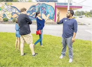  ??  ?? People use a smartphone app to simulate a walk through an artist’s studio outside Sam Flax art supply store during a public walk of the City Unseen art installati­on at locations throughout Orlando.