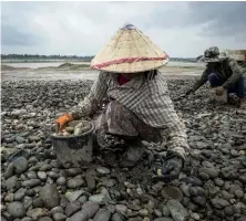  ??  ?? Photo ci-contre : Des travailleu­rs laotiens récoltent des galets sur un site d’extraction de sable le long du Mekong, à Vientiane. La portion laotienne du Mékong est creusée sans relâche pour fabriquer le ciment nécessaire au marché de la constructi­on, en plein boom dans la capitale grâce aux financemen­ts et entreprise­s chinoises. Mais ce dragage détruit peu à peu le cours d’eau, source de revenus vitale pour des centaines de milliers de pêcheurs et paysans dans un pays très touché par la pauvreté en dépit des importante­s ressources naturelles dont il dispose. (© Lillian Suwanrumph­a/AFP)