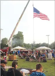  ??  ?? The American flag, suspended from a fire engine, flitters above patriotic people enjoying watermelon, music, family and friends during the 2018 Third of July Celebratio­n.