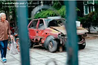  ??  ?? A woman walks past a local relic— a scrapped Xiali model taxi cab