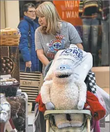  ?? Darrell Sapp/Post-Gazette ?? Barb Wolf of Baldwin Borough pushes her bags from shopping — along with Bumble, the Abominable Snowman from the animated “Rudolph the Red Nose Reindeer” program — on Friday at South Hills Village.