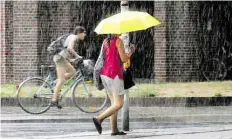  ?? DPA-BILD: HOLLEMANN ?? Eine Frau schützt sich in Hannover unterm Regenschir­m vor dem starken Regen, der Radler wird nass.