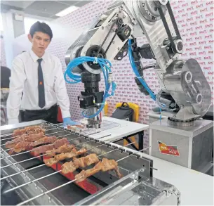  ??  ?? ROBOCHEF: A student watches a robotic machine grilling pork at an exhibition showcasing innovative cooking technology at King Mongkut’s Institute of Technology Ladkrabang in October.