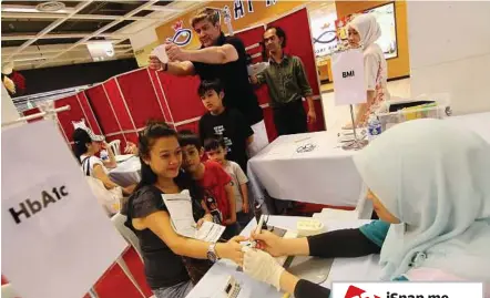  ??  ?? Checking up on health: Jeffrey (in black, background) undergoing a health screening while his wife Alfie Rina (foreground) takes a blood test at the halthcare fair. With them are sons (from left) Mikhail, six, Ameer, three, and Aniq Danial, nine.