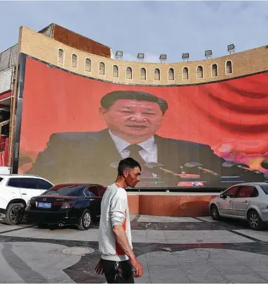  ?? Greg Baker / Getty Images ?? A man walks past a screen showing images of President Xi Jinping in Kashgar in China’s Xinjiang region.