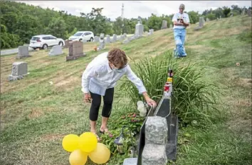  ?? Alexandra Wimley/Post-Gazette ?? Madelyn Roehrig places a copy of her book, "Andy, Can You Hear Us?" against Andy Warhol's tombstone as John Cheezum, of Upper St. Clair, looks on.