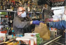  ?? Scott Strazzante / The Chronicle ?? At Noe Hill Market in San Francisco, Duane Stephens wears gloves and mask while he packs a bag of groceries in April.