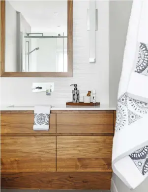  ??  ?? Le mobilier de rangement et le miroir au fini noyer diffusent une chaleur intemporel­le, tandis que le comptoir en quartz avec lavabo sous plan, la céramique finement striée au dosseret et l'applique murale s'inscrivent dans la modernité.