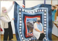  ?? Mona Weatherly ?? Delores Vollenweid­er, center, is shown with her quilt being held by Cecelia Stallbaume­r, left, and Vollenweid­er’s son, Simon at the Oconto American Legion Hall Sunday.