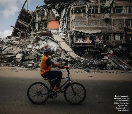  ??  ?? During a ceasefire between Israel and Palestine in May 2021, a child in Gaza City rides past a house destroyed in the fighting