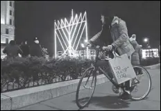  ?? ASSOCIATED PRESS ?? A man on a bicycle pauses Thursday on the first night of Hanukkah, the annual eight-day Jewish festival of lights, on the sidewalk along Fifth Avenue in Manhattan near what has been described as “the world’s largest Hanukkah menorah.”