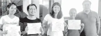  ??  ?? The Impact Volunteer Tutors happily raise their Impact Volunteer Tutor Certificat­es at the orientatio­n program in Barangay Cogon Ramos where they were introduced to the community that they will be serving.