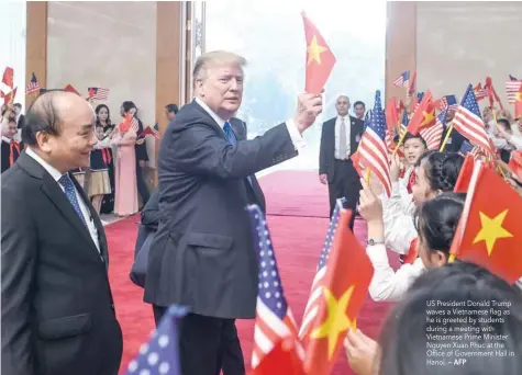  ?? — AFP ?? US President Donald Trump waves a Vietnamese flag as he is greeted by students during a meeting with Vietnamese Prime Minister Nguyen Xuan Phuc at the Office of Government Hall in Hanoi.