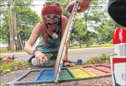  ?? MILLICENT MCKAY/JOURNAL PIONEER ?? Meaghan Roberts spray paints a portion of a rainbow on a local porch step while her husband, Andrew Birch, holds a canvas to stop the blowing fumes from bleeding into the other colours.