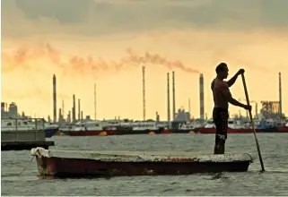  ??  ?? A fisherman rows his dinghy past oil refineries near port terminals in Singapore. (Reuters)