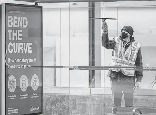  ?? PHOTO BY AZIN GHAFFARI/POSTMEDIA ?? A worker cleans a bus stop with a COVID informativ­e poster attached to it in downtown Calgary last Tuesday.