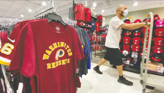  ?? KEVIN LAMARQUE/REUTERS ?? An employee passes Washington Redskins football shirts for sale last week at a sporting goods store in Bailey’s Crossroads, Va. The NFL franchise says it will undertake a “thorough review” of the team name, which critics say is a racial slur. Fedex, a major corporate sponsor, says it had requested that “the team in Washington” change its name.