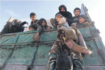  ?? AP ?? A baby is lifted onto a truck carrying civilians fleeing Maaret al-Numan, Syria, ahead of a government offensive on Sunday.