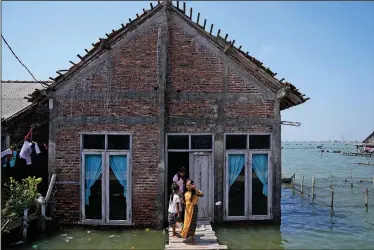  ?? (AP/Dita Alangkara) ?? A family leaves their home surrounded by water July 31 in Timbulslok­o, Indonesia. Some residents of the village have received aid from the local government, but many are still left without a dry place to sleep, afraid a strong tide in the middle of the night could wash them out to sea.