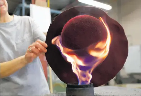  ??  ?? A factory worker applies a felt fedora to the flame. The handmade hats can take weeks to finish.