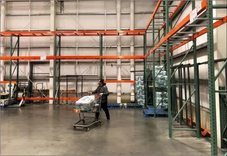  ?? ASSOCIATED PRESS ?? A customer walks past mostly empty shelves on March 2, that normally hold toilet paper and paper towels at a Costco store in Teterboro, N.J. Legions of nervous hoarders are stocking up on canned goods, frozen dinners, toilet paper, and cleaning products. Such hoarding that’s expected to last for weeks has created big challenges for discounter­s and grocery stores as well as food delivery services.