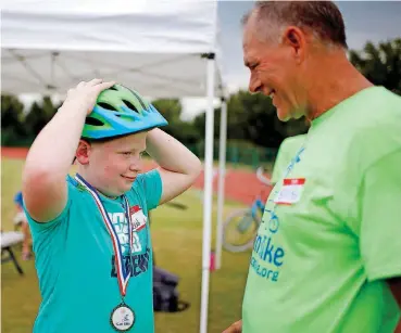  ?? [PHOTO BY SARAH PHIPPS, THE OKLAHOMAN] ?? Reid Martin gets a medal from Bob Rook during the iCan Bike Camp.