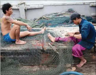  ?? NICOLAS ASFOURI/AFP ?? Migrant workers repair a net on a Thai fishing boat in Thailand’s Rayong province. Thousands of Cambodians board similar boats every day, but many are slaves forced to work in grueling conditions.