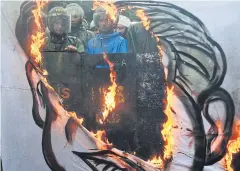  ?? AFP ?? Riot police look on past a burning banner with a representa­tion of late dictator Ferdinand Marcos near the Heroes Cemetery in Manila yesterday.