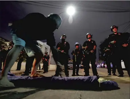  ?? Luis Sinco Los Angeles Times ?? A HOMELESS MAN lays out a bedroll in front of officers near Echo Park Lake on the night of March 24. Two council members seek answers from the LAPD on costs for the Echo Park deployment — including officer pay, overtime costs, equipment and helicopter expenses.