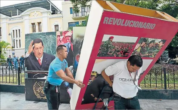  ?? RONALDO SCHEMIDT / AFP ?? Empleados de la Asamblea Nacional venezolana retiran del edificio imágenes del desapareci­do presidente Hugo Chávez