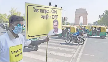  ?? — AFP photo ?? A civil defence volunteer holds a placard on a busy road during an initiative taken by Delhi government asking commuters to switch-off the ignition of their vehicles at traffic red lights in order to control pollution levels near India Gate in New Delhi.