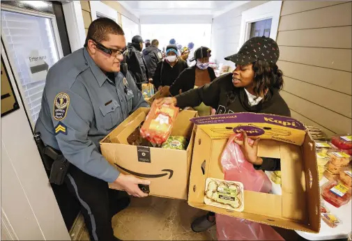  ?? PHOTOS BY MIGUEL MARTINEZ/MIGUEL.MARTINEZJI­MENEZ@AJC.COM ?? Community affairs Officer Christian Matos of the Gwinnett Police Department helps box food for Tiffany Miller at the Bradford Gwinnett apartment complex near Norcross during a community outreach event Feb. 2.